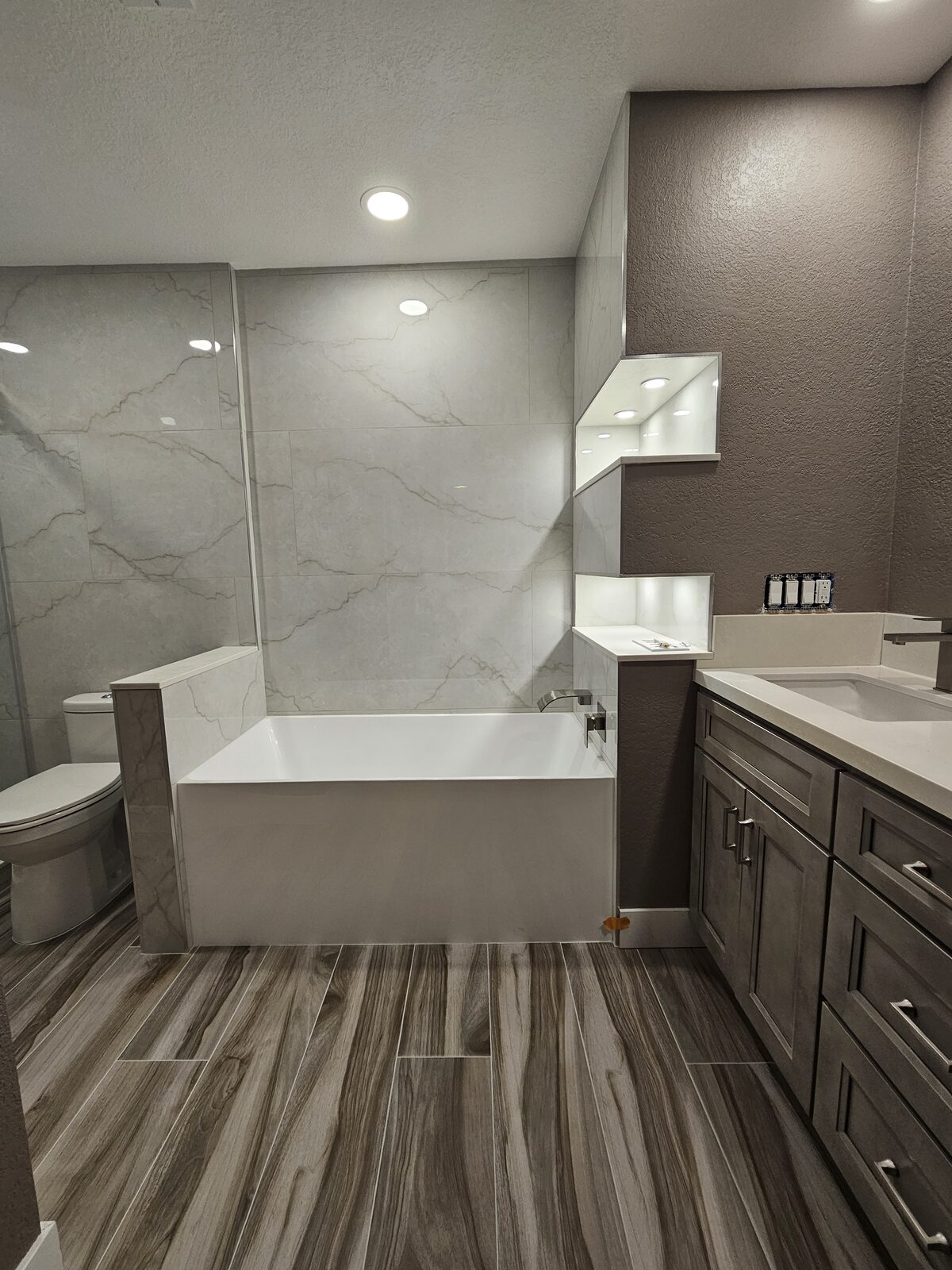 Bathroom remodel with large-format marble-look porcelain, drop-in tub, lit display niches and wood-look tile flooring